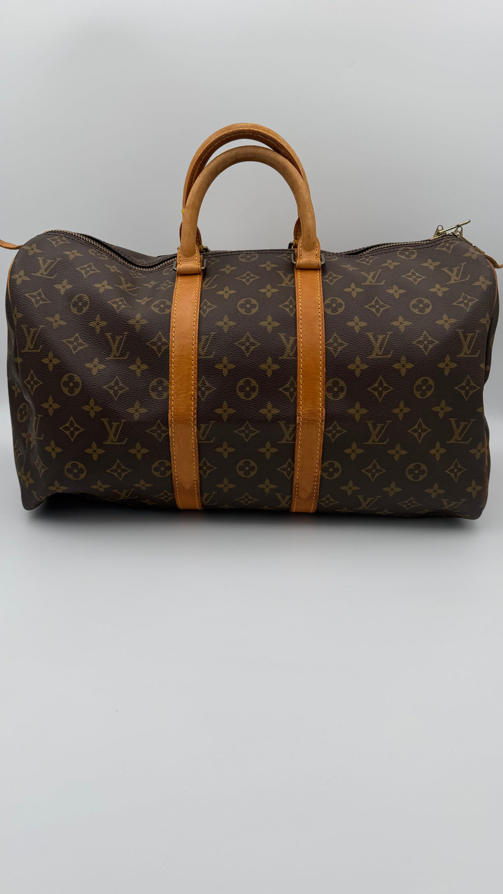 Brown monogram duffel bag with tan leather straps on a light gray background