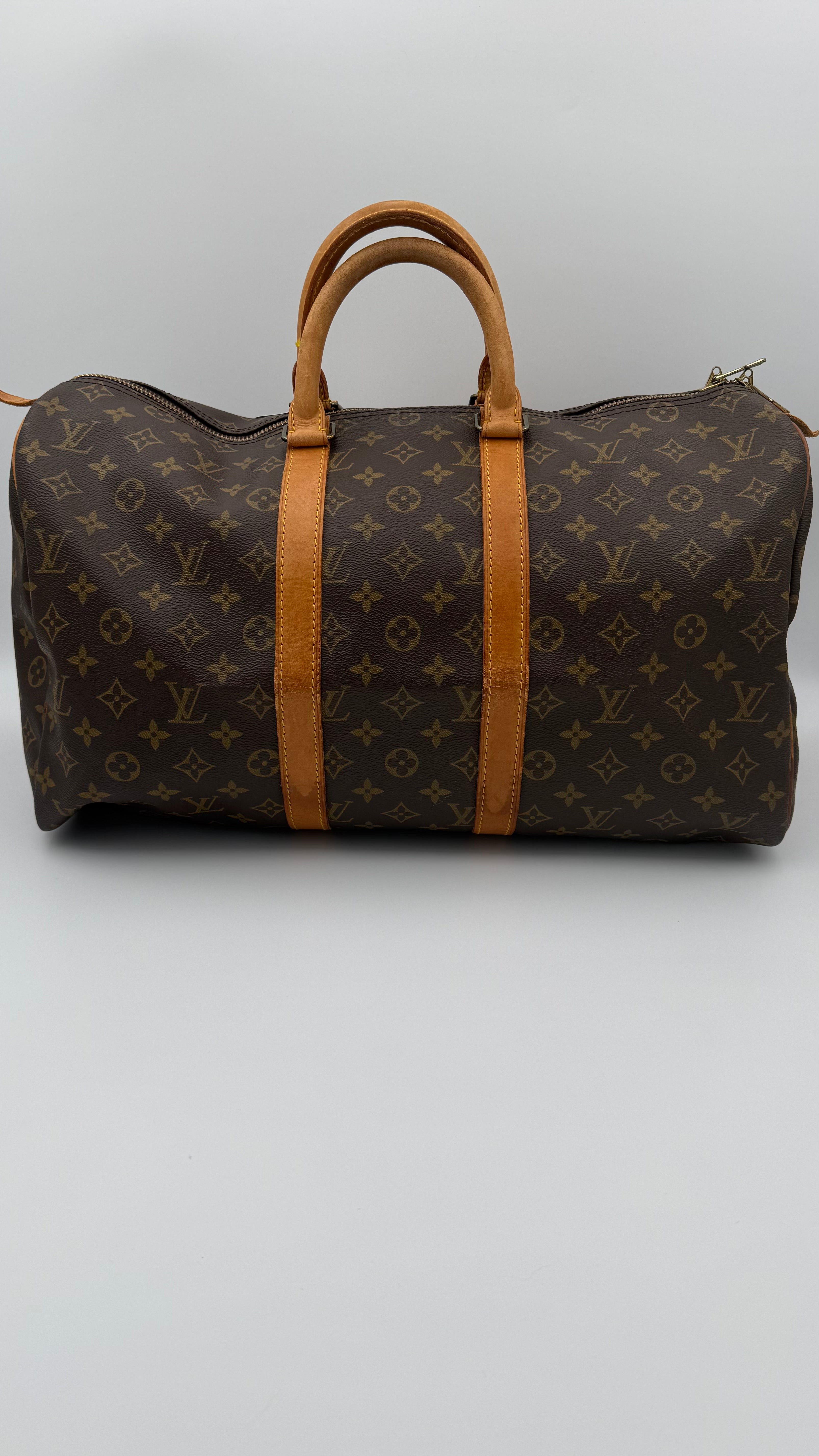 Brown monogram duffel bag with tan leather straps on a light gray background