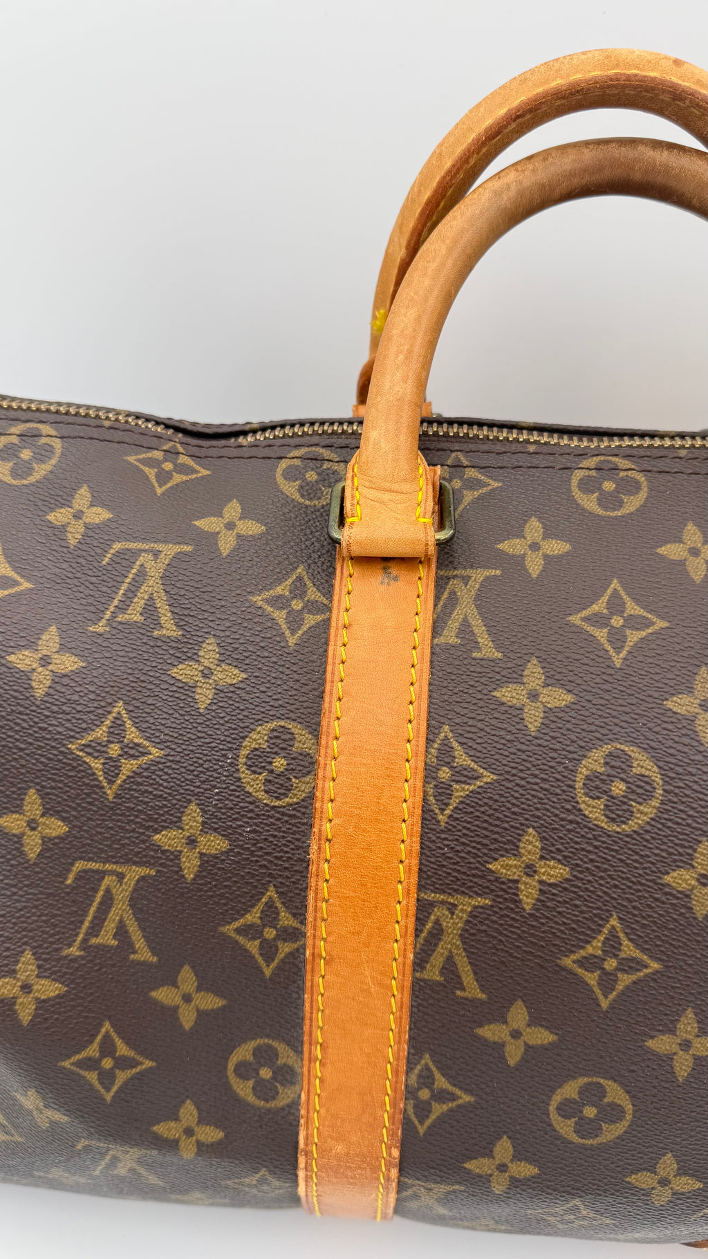Brown duffel bag with tan handles and monogram pattern on a white background