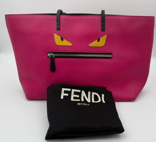 Pink tote bag with cartoonish eyes and a black Fendi pouch on a white background